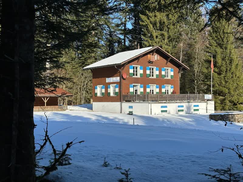 Das Berghaus Ricketschwändi im Winter, umgeben von verschneiten Tannen